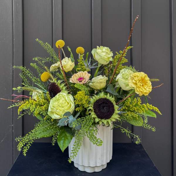 Green and yellow floral arrangement in a white vase