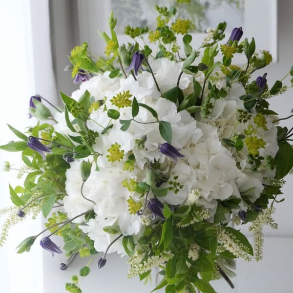White hydrangea bouquet with purple bell-shaped flowers and green accents