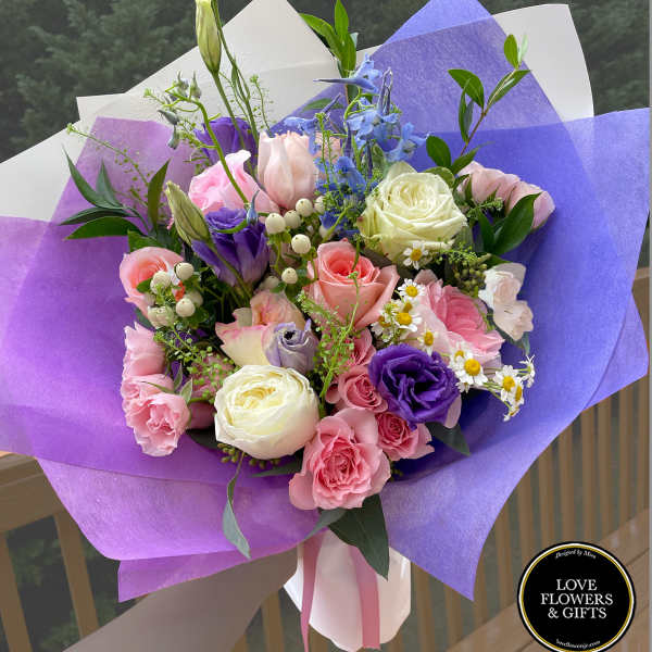 Hand-tied bouquet of pink roses, purple lisianthus, and white blooms wrapped in purple and white paper