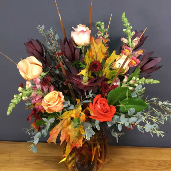 Autumn bouquet of roses and snapdragons in an amber glass vase