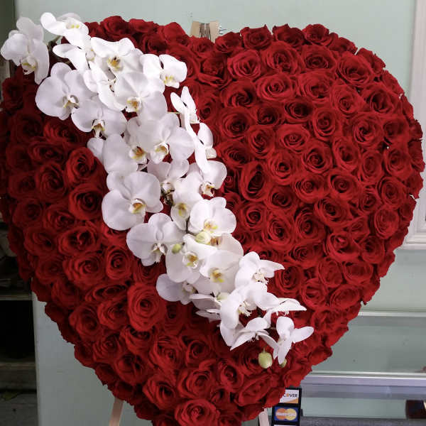 Heart-shaped red rose arrangement with white orchids across the front