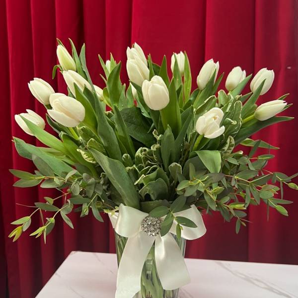 White tulips arranged in a clear glass vase with a white ribbon
