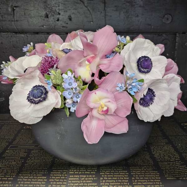 Pink orchids and white anemones arranged in a dark bowl