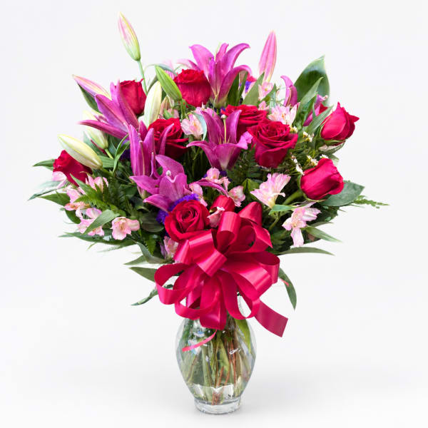 Bouquet of pink lilies and red roses in a clear glass vase with a pink ribbon