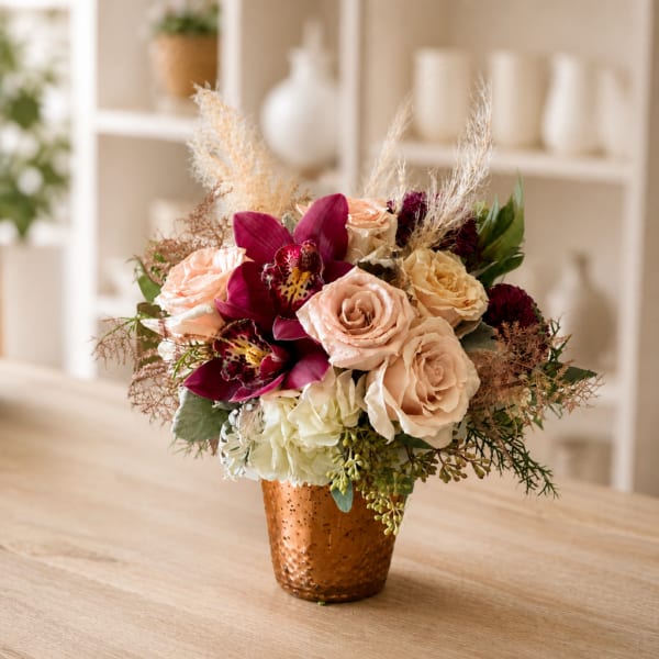 Bouquet of blush roses and deep magenta orchids in a copper vase