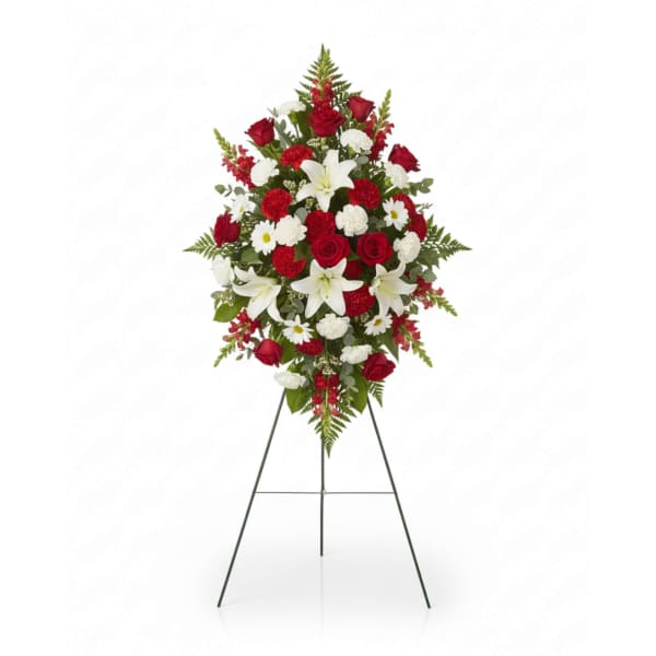 Standing floral spray with red roses, white lilies, and white daisies on an easel