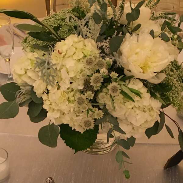 White floral centerpiece in a clear glass vase with eucalyptus