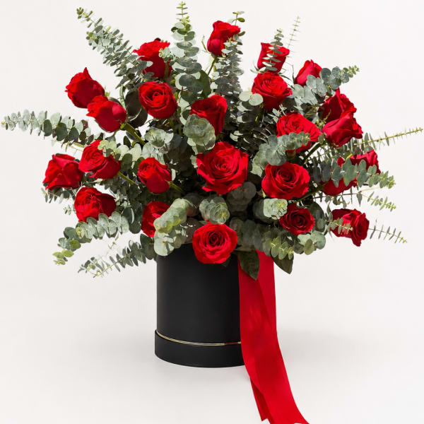 Red roses in a black hatbox with eucalyptus and a red ribbon