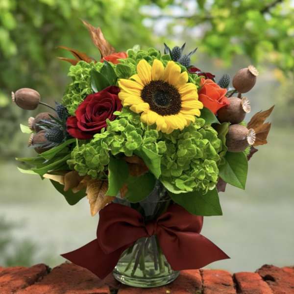 Bouquet with a sunflower, red and orange roses, and green hydrangeas in a glass vase