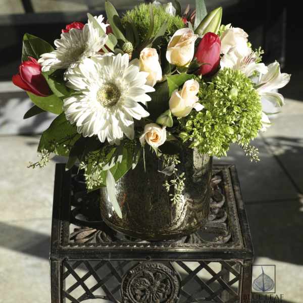 Bouquet of white daisies, pale roses, and red tulips in a glass vase
