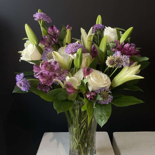 Bouquet of white lilies, roses, and purple flowers in a glass vase