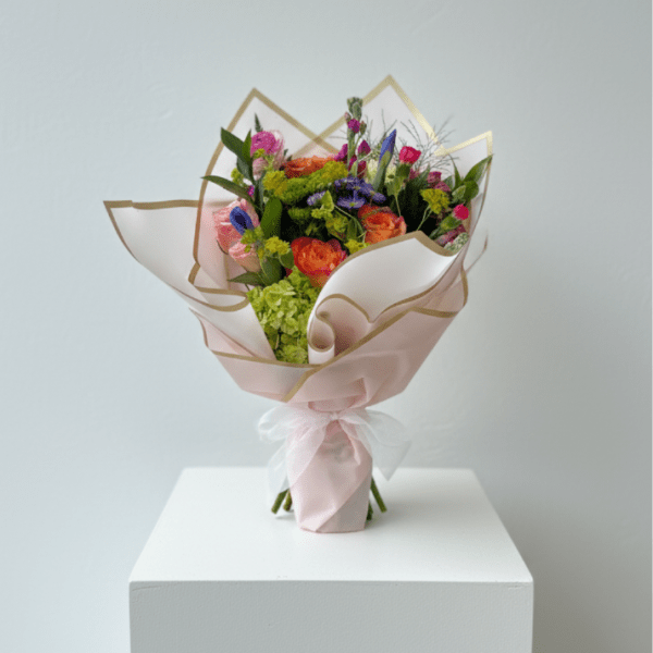 Bouquet of orange, pink, and purple flowers wrapped in pale pink paper