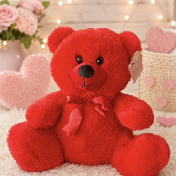 Red plush teddy bear with a satin bow sitting on a soft blanket