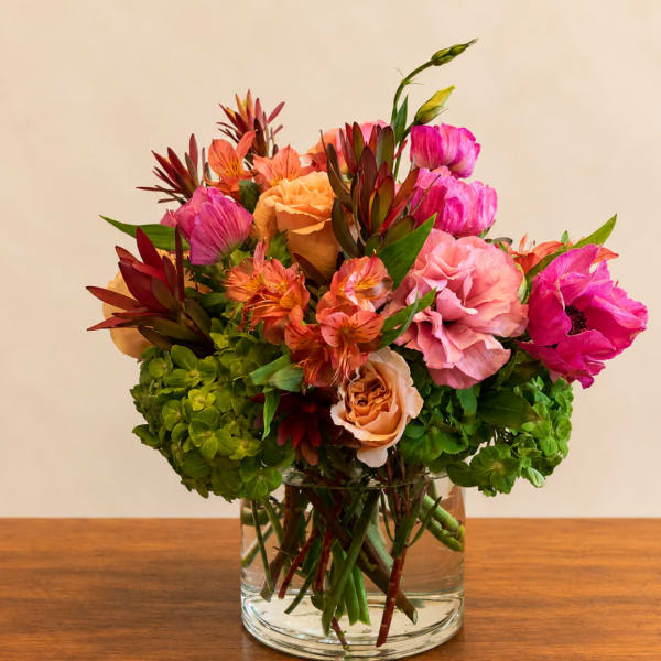 Mixed bouquet of pink, peach, and orange flowers in a clear glass vase