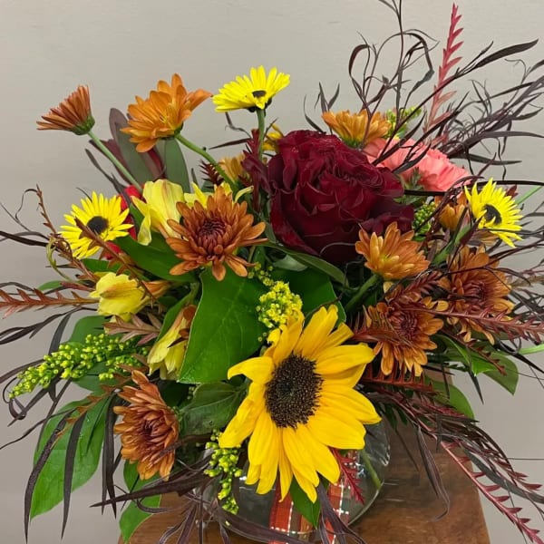 Mixed bouquet with a red rose, sunflowers, and orange daisies in a glass vase