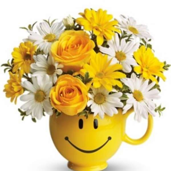 Yellow smiley-face mug holding yellow roses and white daisies