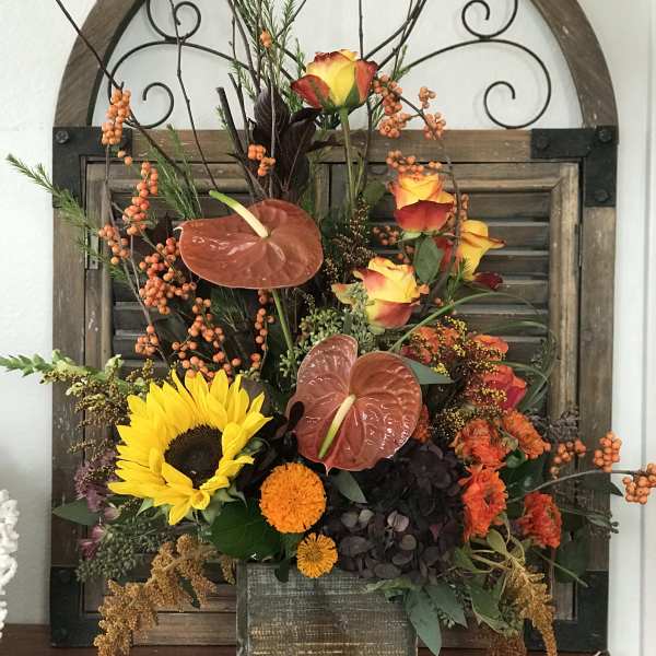 Mixed autumn floral arrangement with sunflowers, roses, and anthuriums in a wooden container