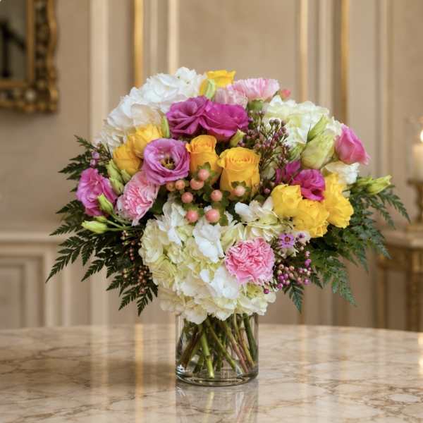 Mixed bouquet of pink, yellow, and white flowers in a clear glass vase