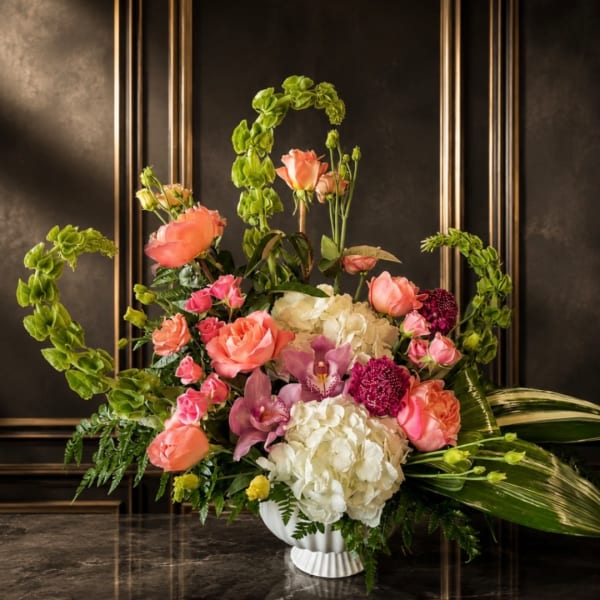 Pink and white floral arrangement in a white vase with tall green accents
