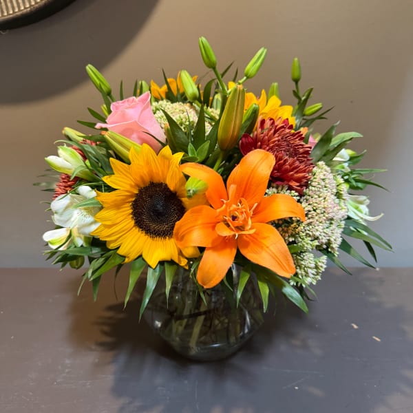 Mixed bouquet with sunflower, orange lily, and pink rose in a glass vase