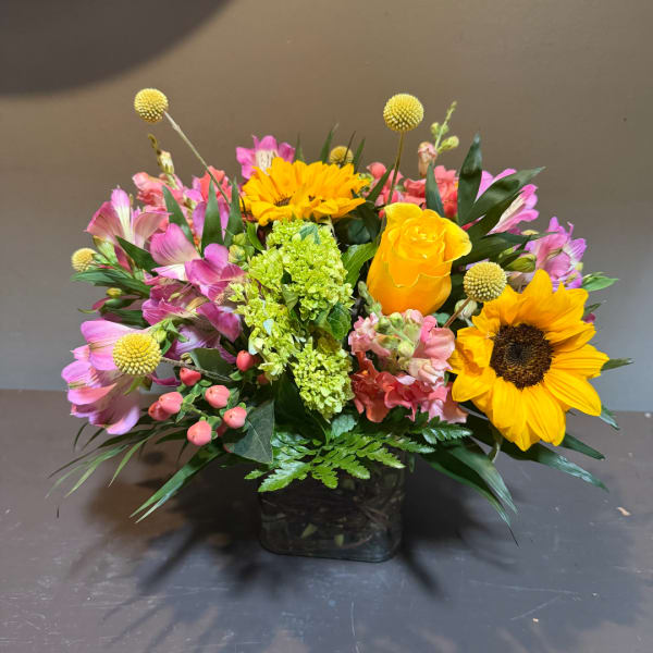 Mixed bouquet with sunflowers, yellow roses, and pink flowers in a square vase