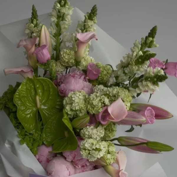 Bouquet of pink lilies, calla lilies, and pale green hydrangeas wrapped in white paper