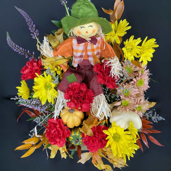 Scarecrow decoration surrounded by yellow, red, and pink flowers