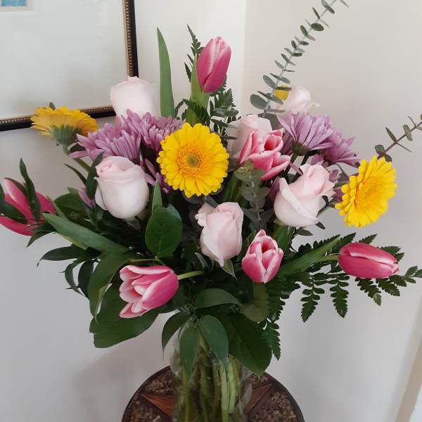 Mixed bouquet of pink tulips, pale roses, and yellow daisies in a glass vase