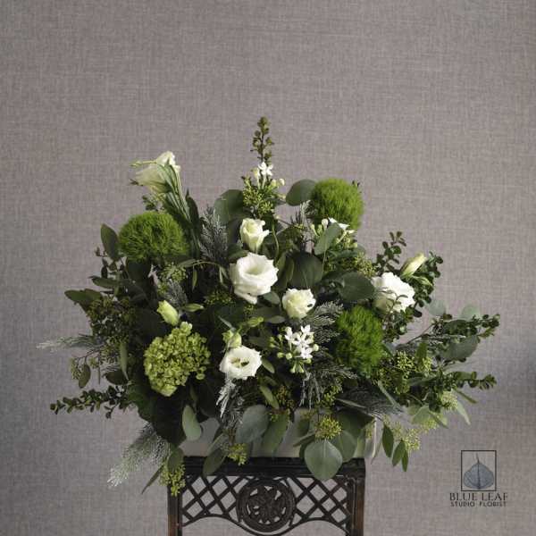 White flowers and green blooms arranged in a low container on a decorative stand