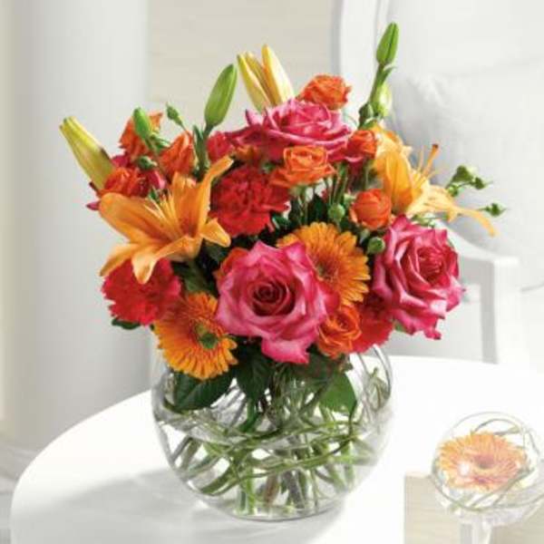 Bouquet of pink roses, orange lilies, and gerbera daisies in a glass vase