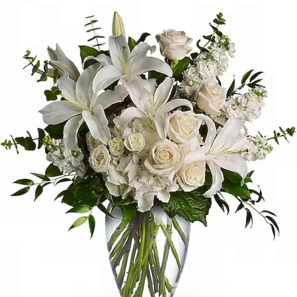 White lilies, roses, and hydrangeas arranged in a clear glass vase.