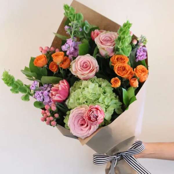 Hand-tied bouquet of pink, orange, and green flowers wrapped in paper