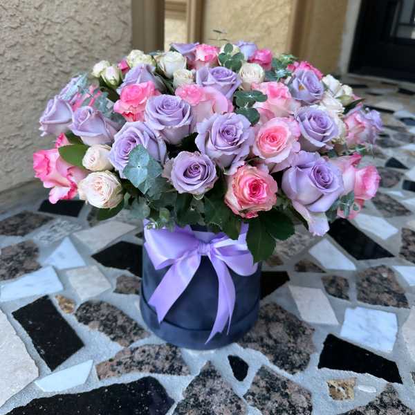 Lavender and pink roses arranged in a round box with a ribbon