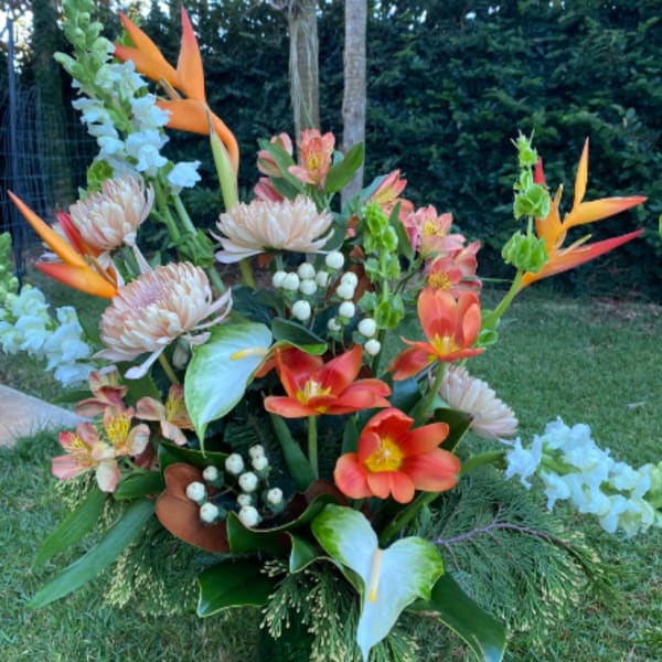 Tropical floral arrangement with orange birds of paradise and coral blooms in a green vase