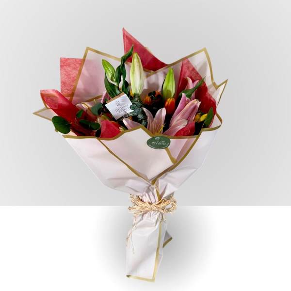 Bouquet of pink and white lilies wrapped in white paper with gold trim