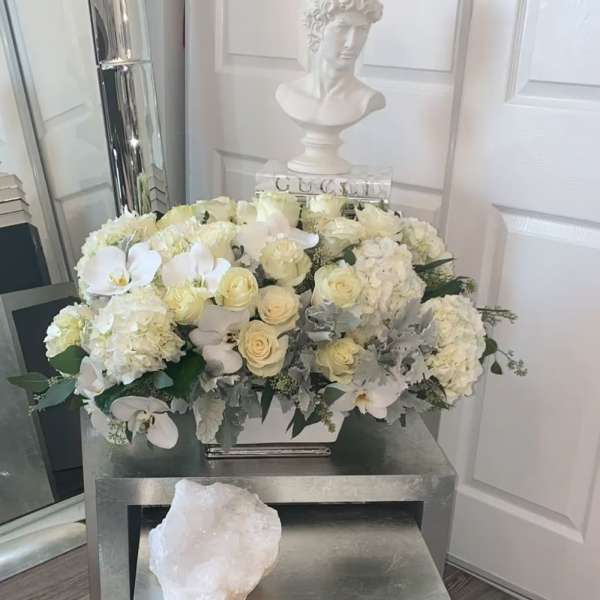 White floral arrangement with roses, hydrangeas, and orchids in a rectangular container