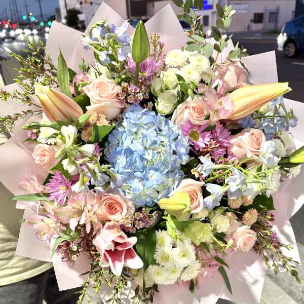 Mixed bouquet with blue hydrangea, pink roses, lilies, and daisies in pink wrap