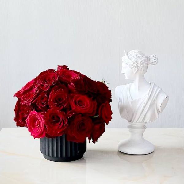 Red rose bouquet in a black vase beside a white bust sculpture