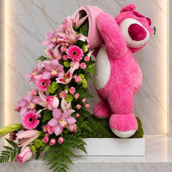 Pink floral arrangement with a large pink teddy bear in a white planter