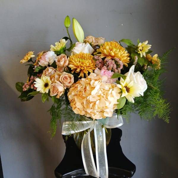 Mixed bouquet of peach, white, and yellow flowers in a glass vase with ribbon