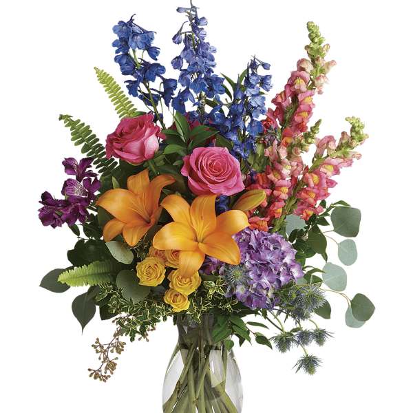 Colorful mixed bouquet in a clear glass vase with lilies, roses, and blue flowers