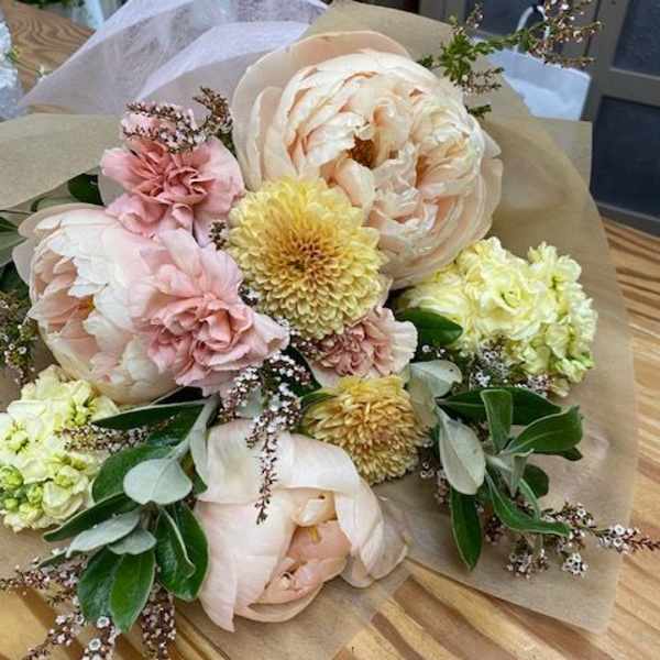 Pastel bouquet with large blush peonies and yellow blooms wrapped in paper