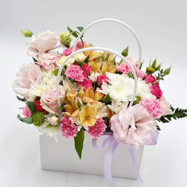 Pastel flower arrangement in a white handled box with a lavender ribbon