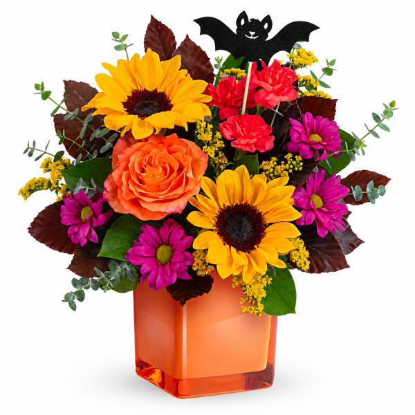 Orange and yellow flowers in an orange glass vase with a bat decoration
