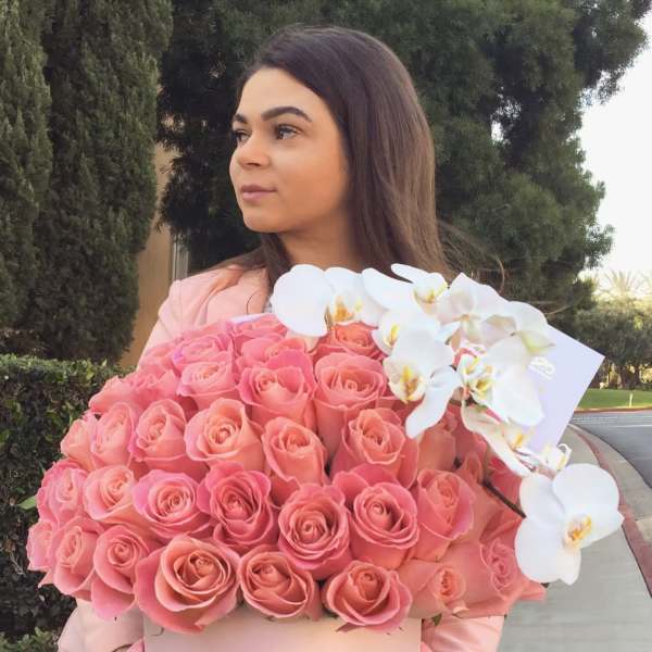 Woman holding a large pink rose box with white orchids