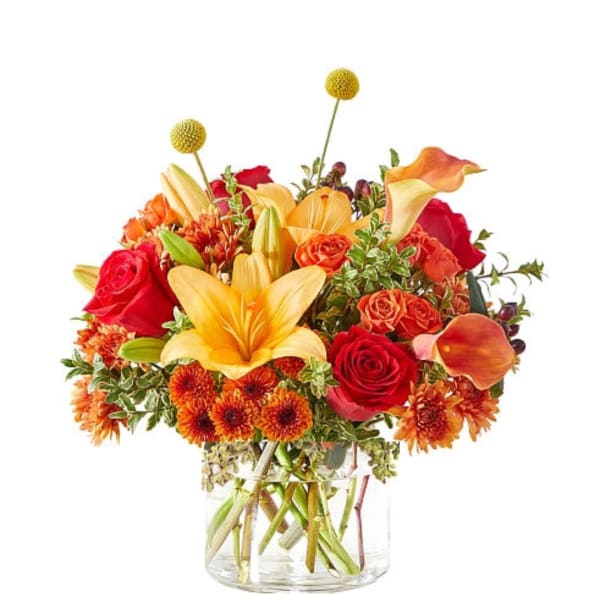 Bouquet of red roses, orange lilies, and yellow pom flowers in a clear glass vase