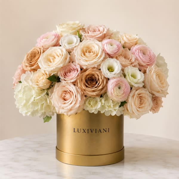 Pastel roses and ranunculus arranged in a gold hatbox