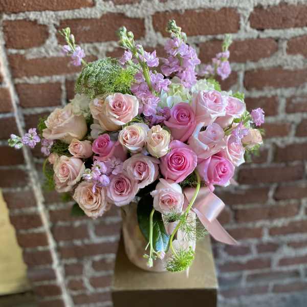 Pink and peach rose arrangement with soft pink accent flowers in a blush vase with ribbon