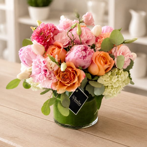 Pink and orange flower arrangement in a green glass vase