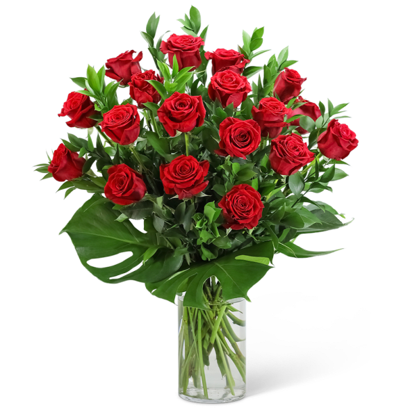 Red roses arranged in a clear glass vase with broad green leaves